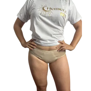 Mujer posando con ropa interior menstrual color nude, ideal para usar con pantalón blanco o uniforme, y camiseta blanca con el logotipo de Hemeranix.